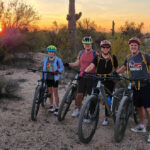 A family of four pauses during one of the Phoenix mountain bike tours from the Wild Bunch with a trademark Arizona sunset in the background.