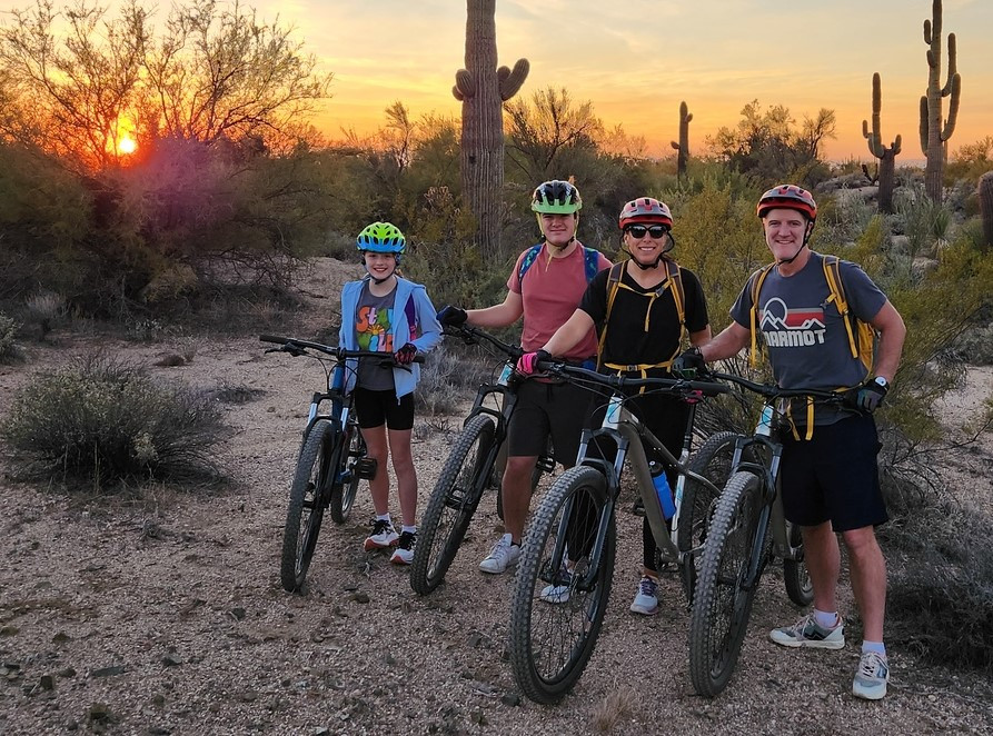 A family of four pauses during one of the Phoenix mountain bike tours from the Wild Bunch with a trademark Arizona sunset in the background.