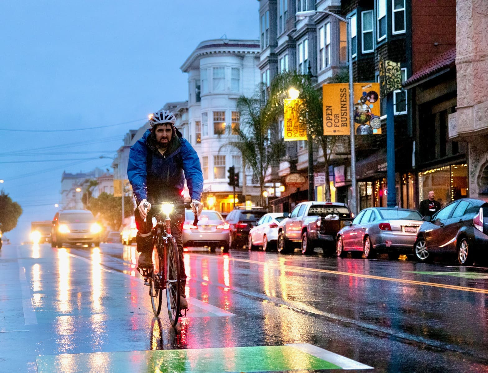 A person riding a bicycle towards the camera in a bike lane wearing full rain gear.