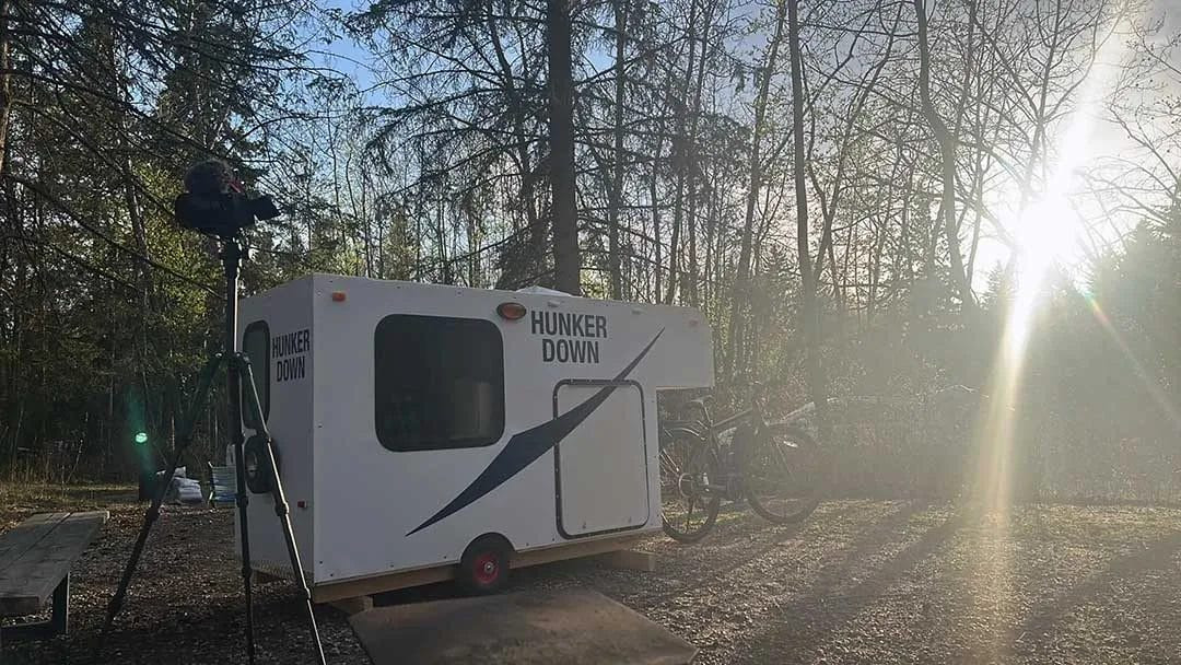 The DIY bike trailer camper at its first campsite in a wooded area, illustrating its practical use in a natural setting.