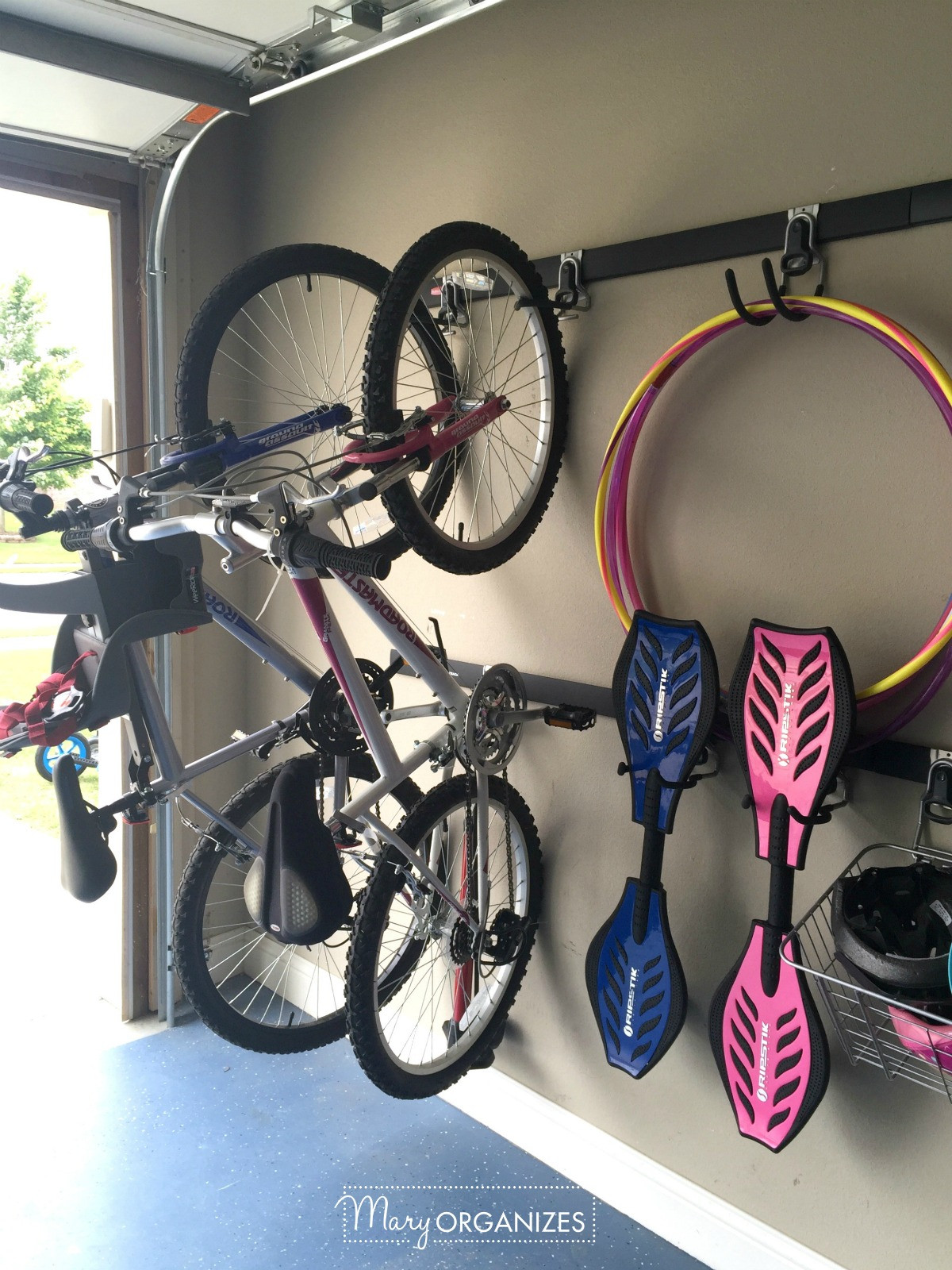 Two adult bikes hanging on wall mounted hooks in a garage, with a bike pump hanging between them.