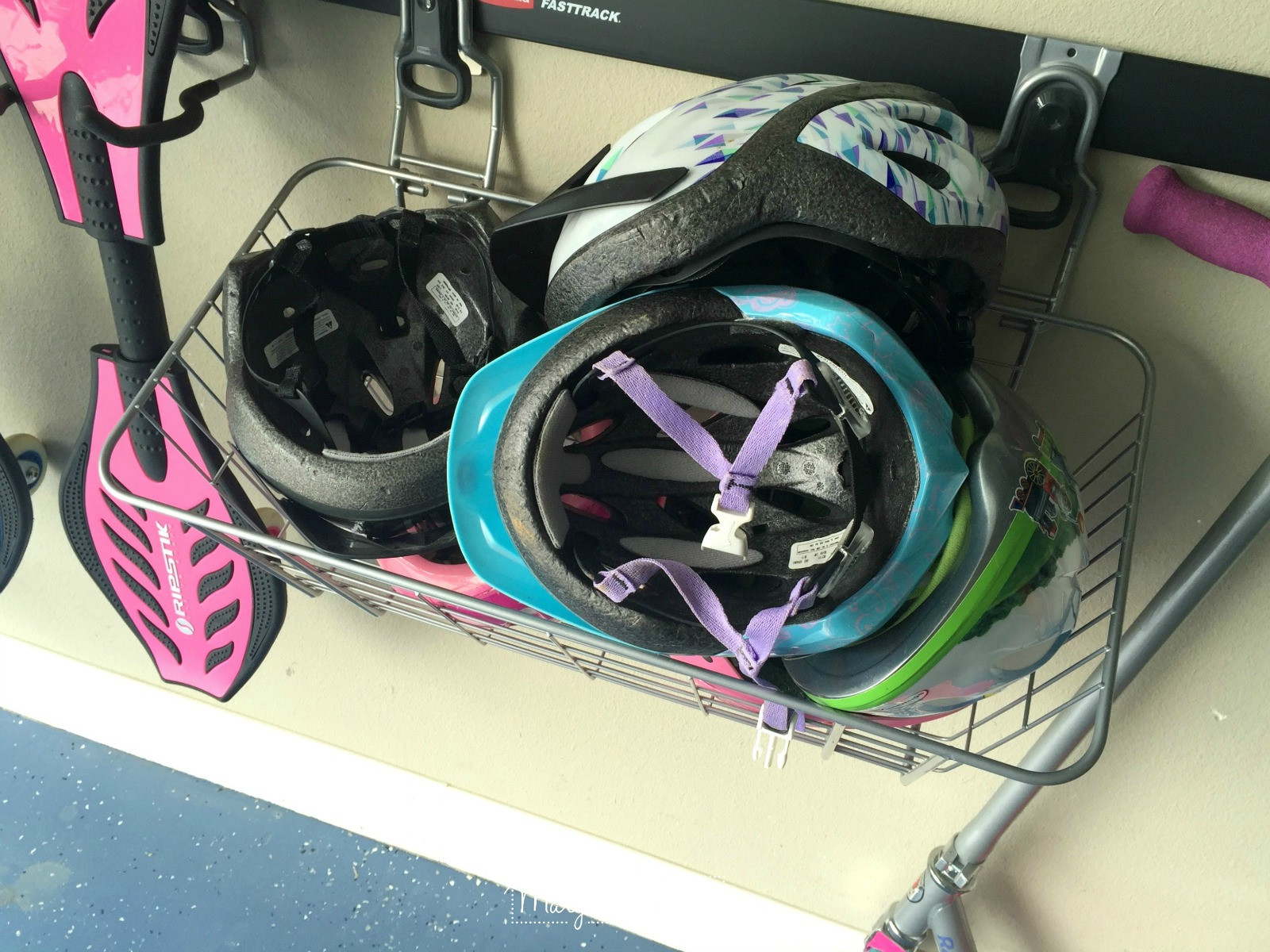 Bike helmets hanging in a basket on a FastTrack system in a garage.