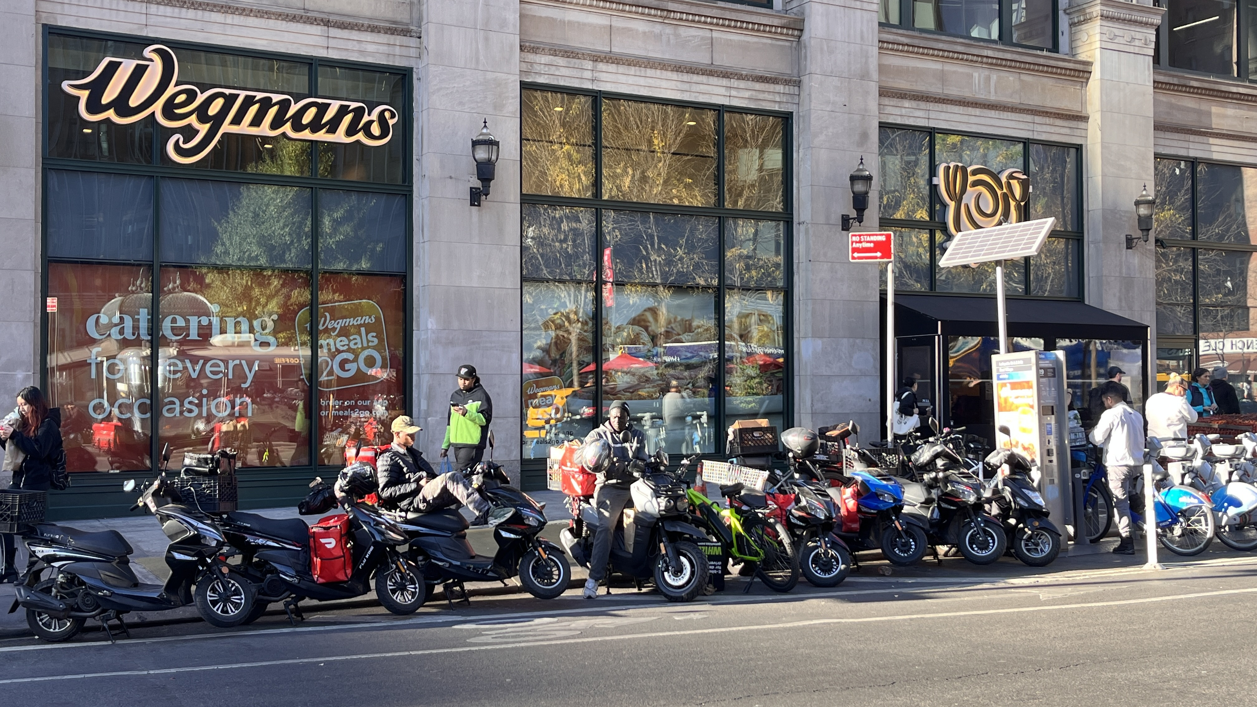 Whizz e-bikes and other delivery mopeds parked outside Wegmans in East Village Manhattan, illustrating the demand for e-bike rentals in NYC.