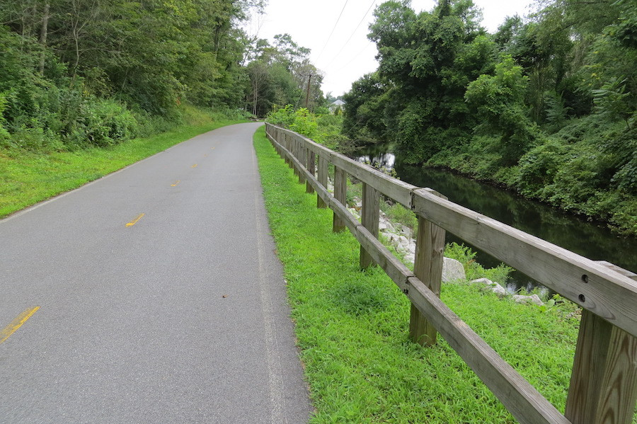 The Fred Lippitt Woonasquatucket River Greenway in Rhode Island, featuring a paved section of the trail alongside the river in an urban setting