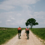 Rider silhouetted against a sunset sky, riding a single speed gravel bike on a dirt road.