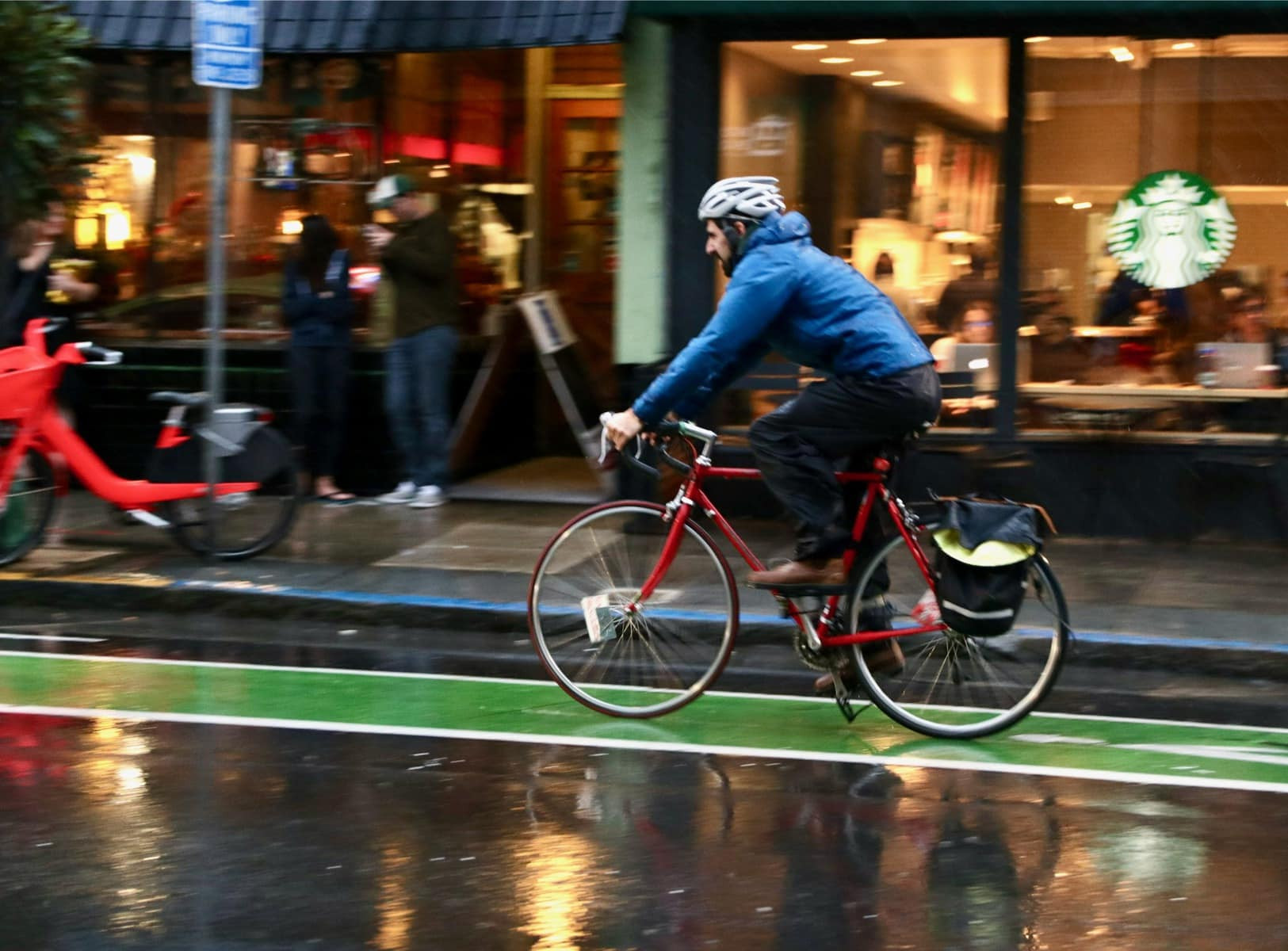 A person on a road bicycle riding in a bike lane with a wet road and a light drizzle. There