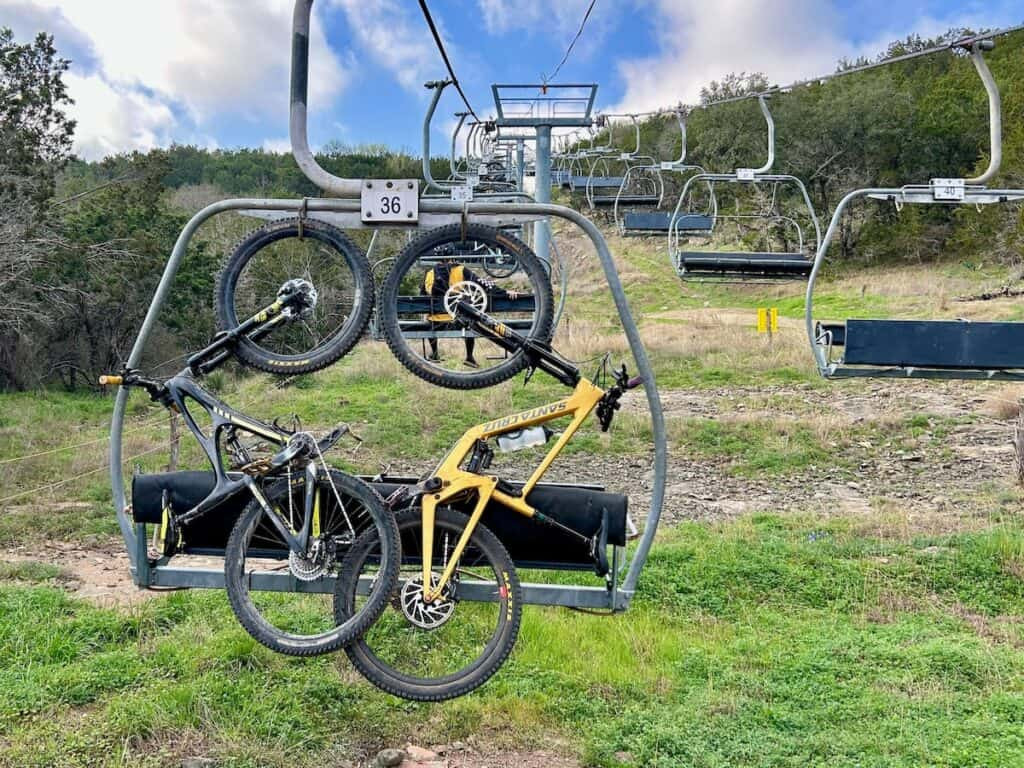 Mountain bikes securely loaded onto chairlift hooks at Spider Mountain Bike Park, Texas