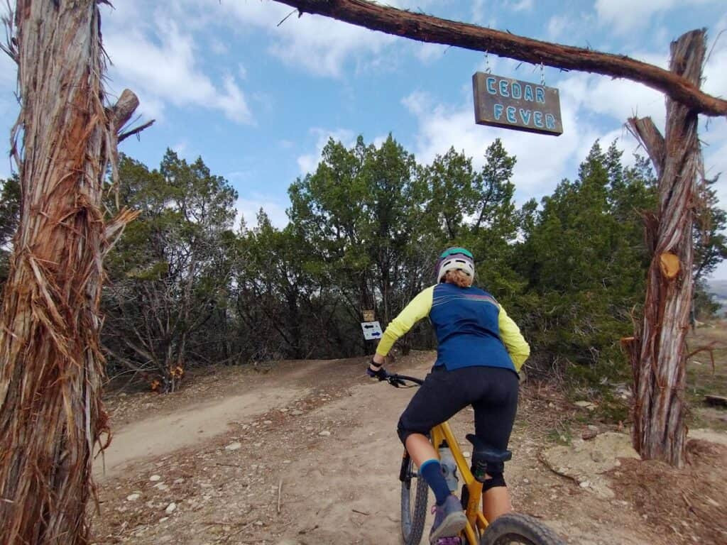 A mountain biker pauses under the Cedar Fever trail sign at Spider Mountain Bike Park, Texas