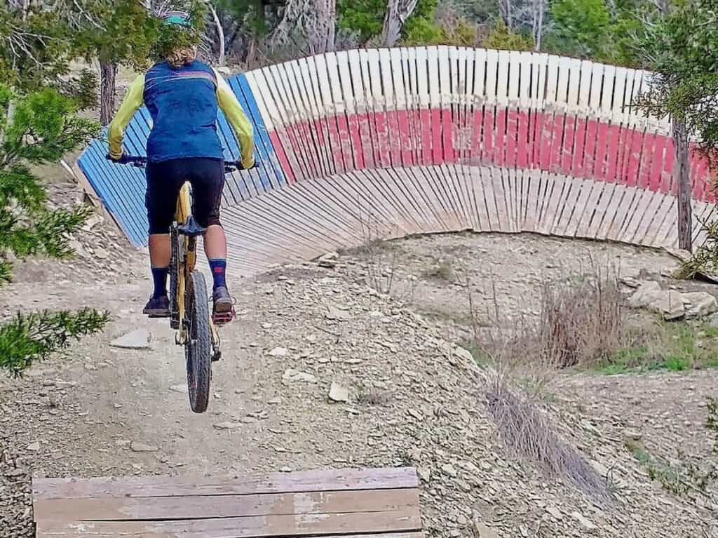Mountain biker executes a jump in front of the iconic Texas flag wall ride at Spider Mountain Bike Park, Texas