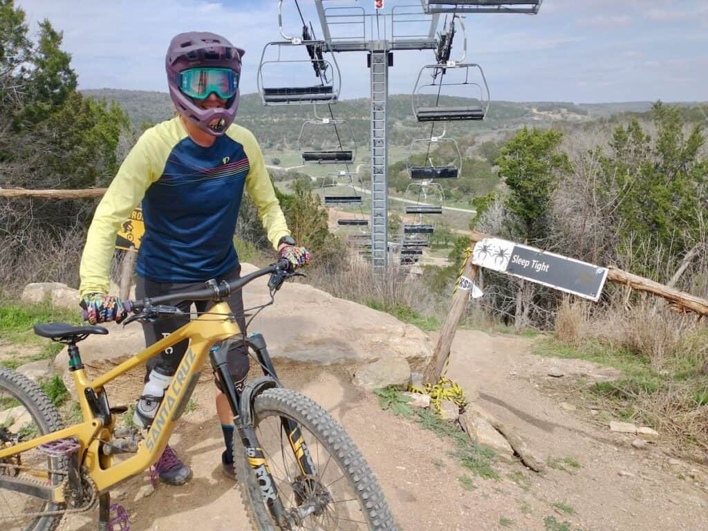 A happy mountain biker in a full face helmet stands with their bike at Spider Mountain Bike Park, Texas, after a great day of riding