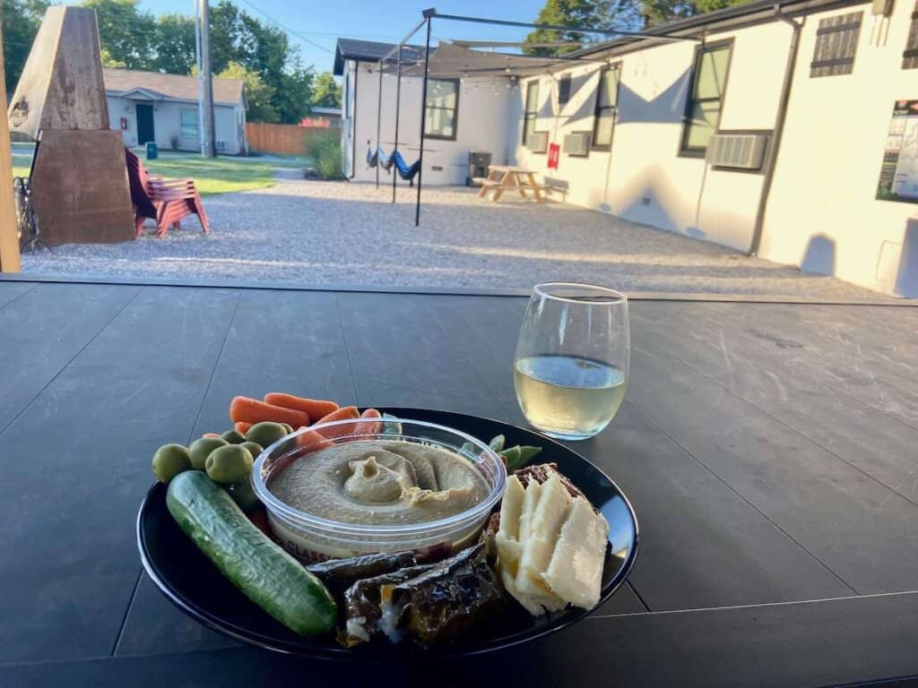 Plate of hummus, vegges, and cheese and glass of white wine on table in backyard of the Bike Inn Bentonville