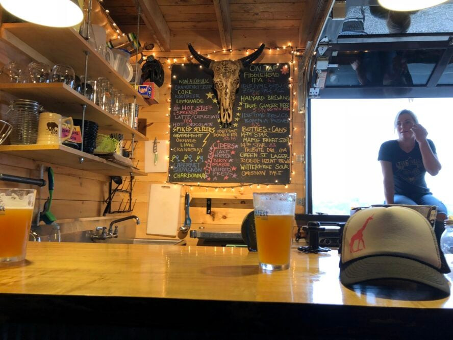 Enjoying a post-ride beer at a trailside bar in Kingdom Trails, emphasizing the social and relaxing aspects of mountain biking in the region, perfect for unwinding after a beginner ride.