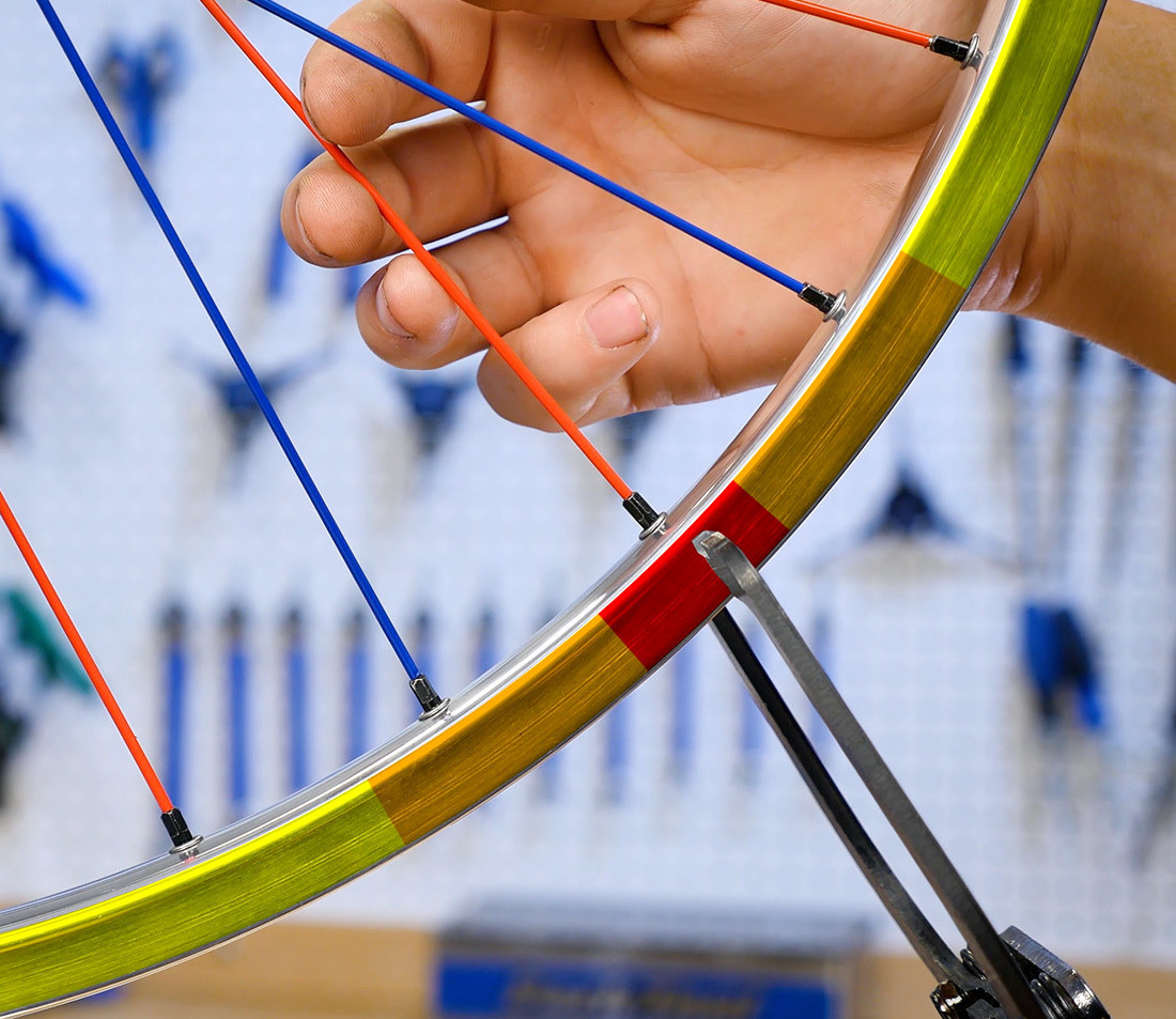 Bicycle wheel in truing stand with red, orange, and yellow highlights radiating from a spoke