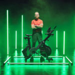 Man in a red shirt standing behind a RE:GEN bike in a green-lit studio