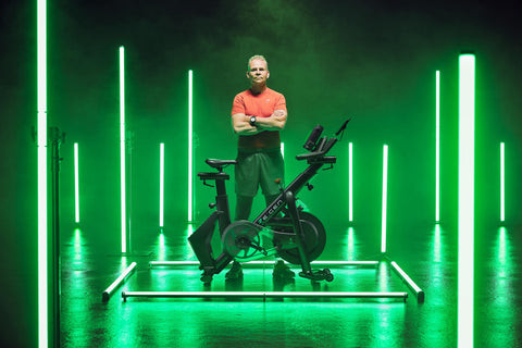 Man in a red shirt standing behind a RE:GEN bike in a green-lit studio