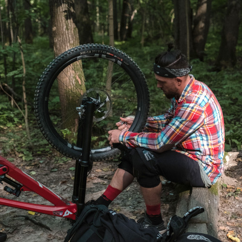 Mountain biker fixing spokes on his wheel, taking a break on a log
