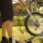 Cyclist using a garden hose to rinse off loose dirt from an electric bike