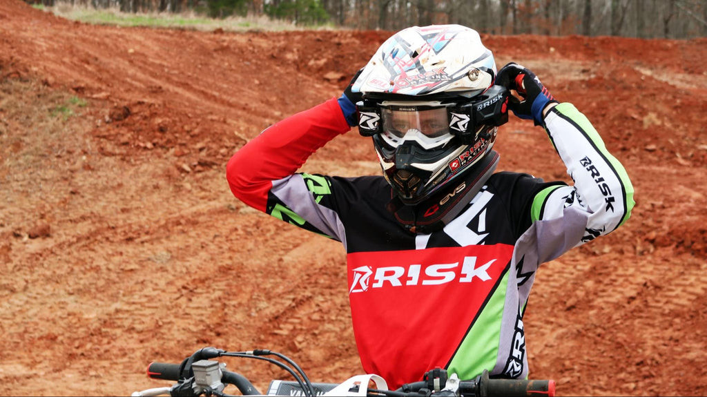 A young motocross rider checking his goggles, highlighting the focus and gear required for the sport