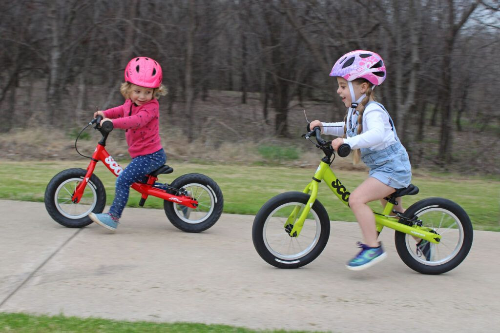 Two girls on balance bikes racing each other. A 2 year old is on the Ridgeback Scoot. The 4 year old is on the Ridgeback Scoot XL.